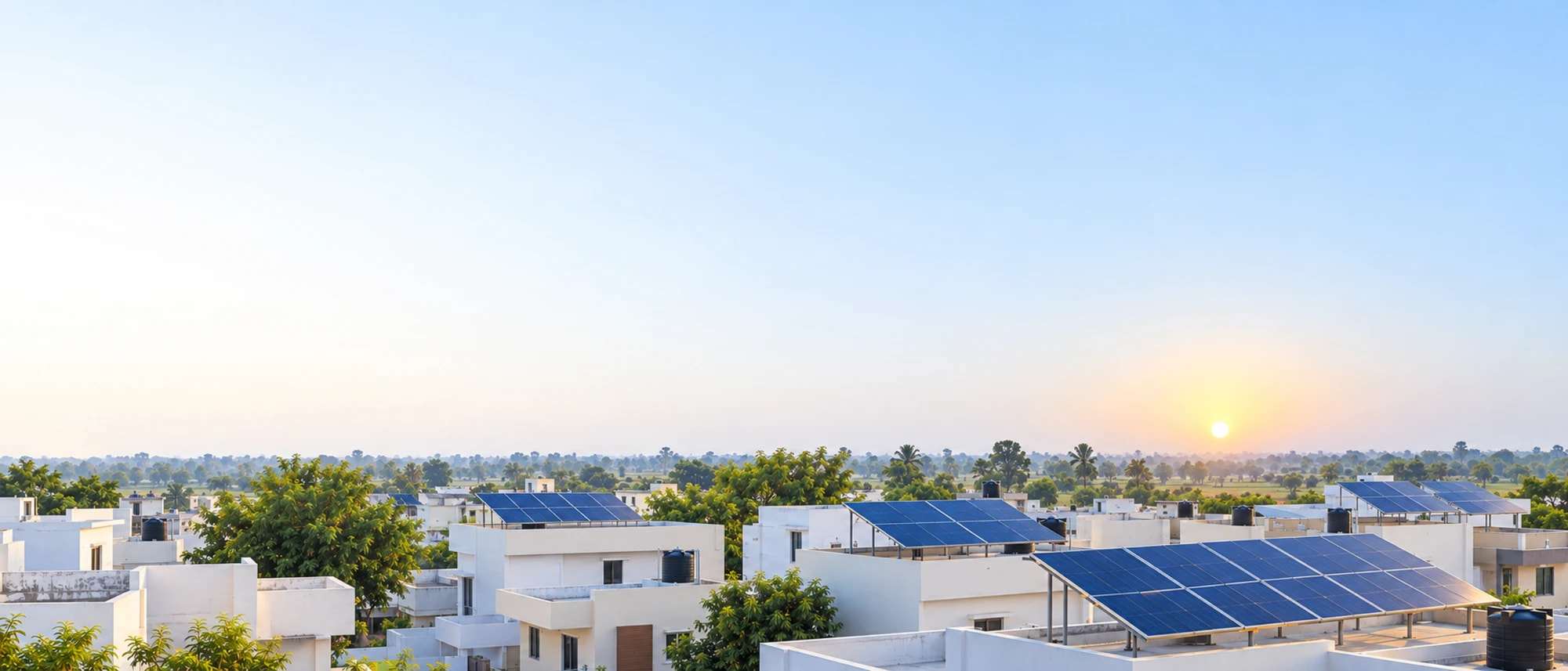 Sunrise over the flat rooftops of a small North Indian town, with solar panels on several houses.